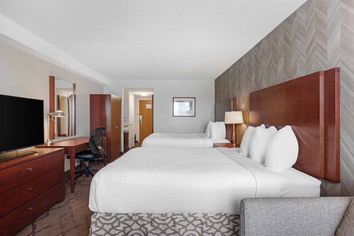 Ein Hotelzimmer mit einem großen Bett, einem Schreibtisch mit Flachbildfernseher, einem Sessel und einem Kleiderschrank.