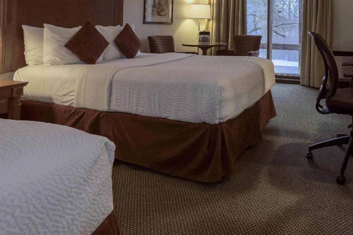 Ein Hotelzimmer mit einem großen Bett, einem kleineren Bett, einem Schreibtisch, einem Stuhl und einem Fenster mit Blick.