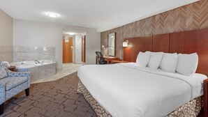 Una habitación de hotel con una cama grande, una zona de estar con una silla, un escritorio y una bañera.