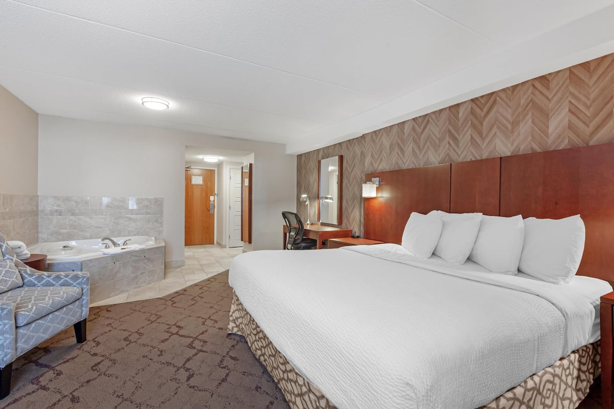 Ein Hotelzimmer mit einem großen Bett, einer Sitzecke mit einem Sessel, einem Schreibtisch und einer Badewanne.