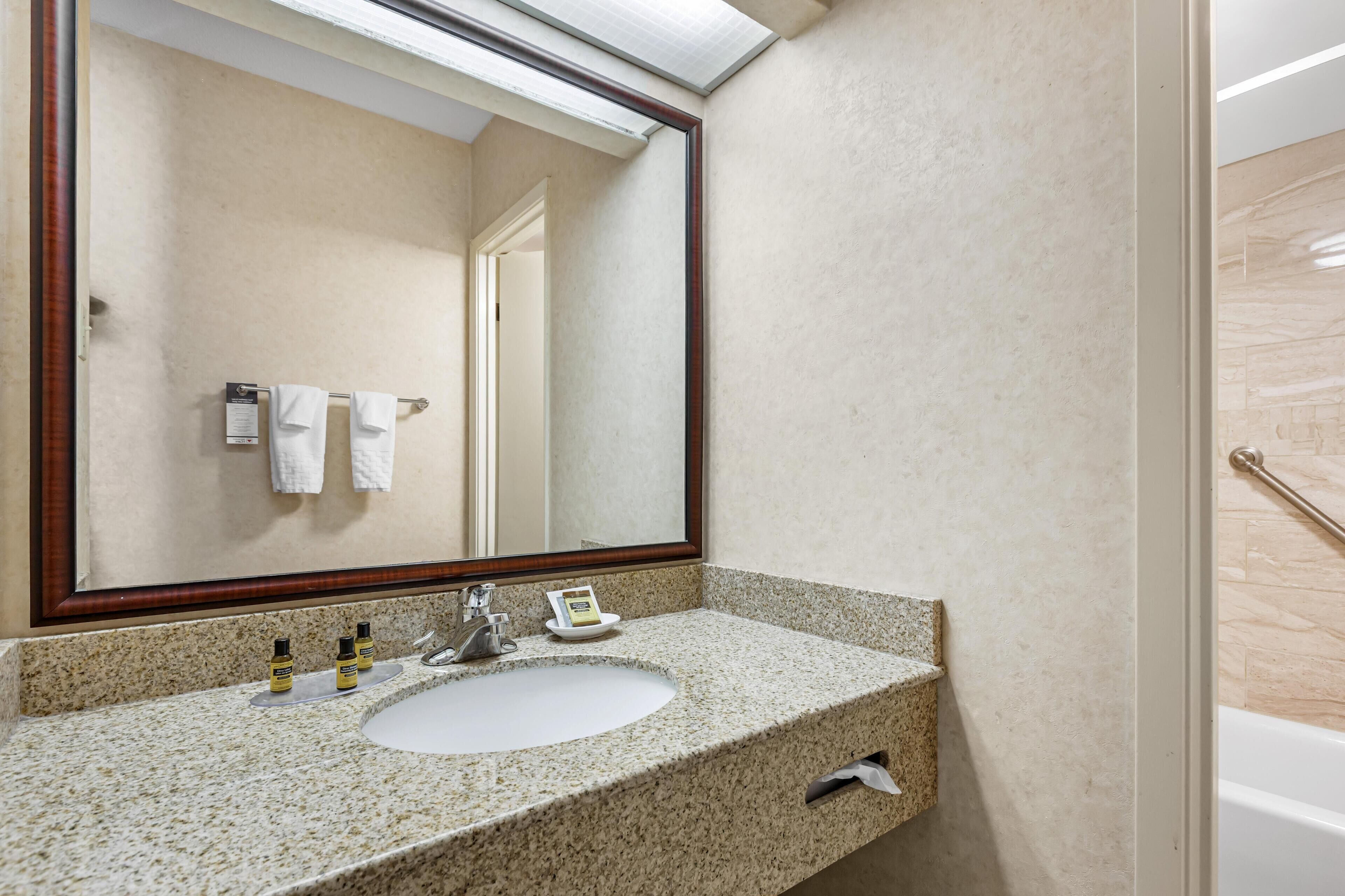 A bathroom with a granite countertop sink, a mirror, and a hand sanitizer dispenser.