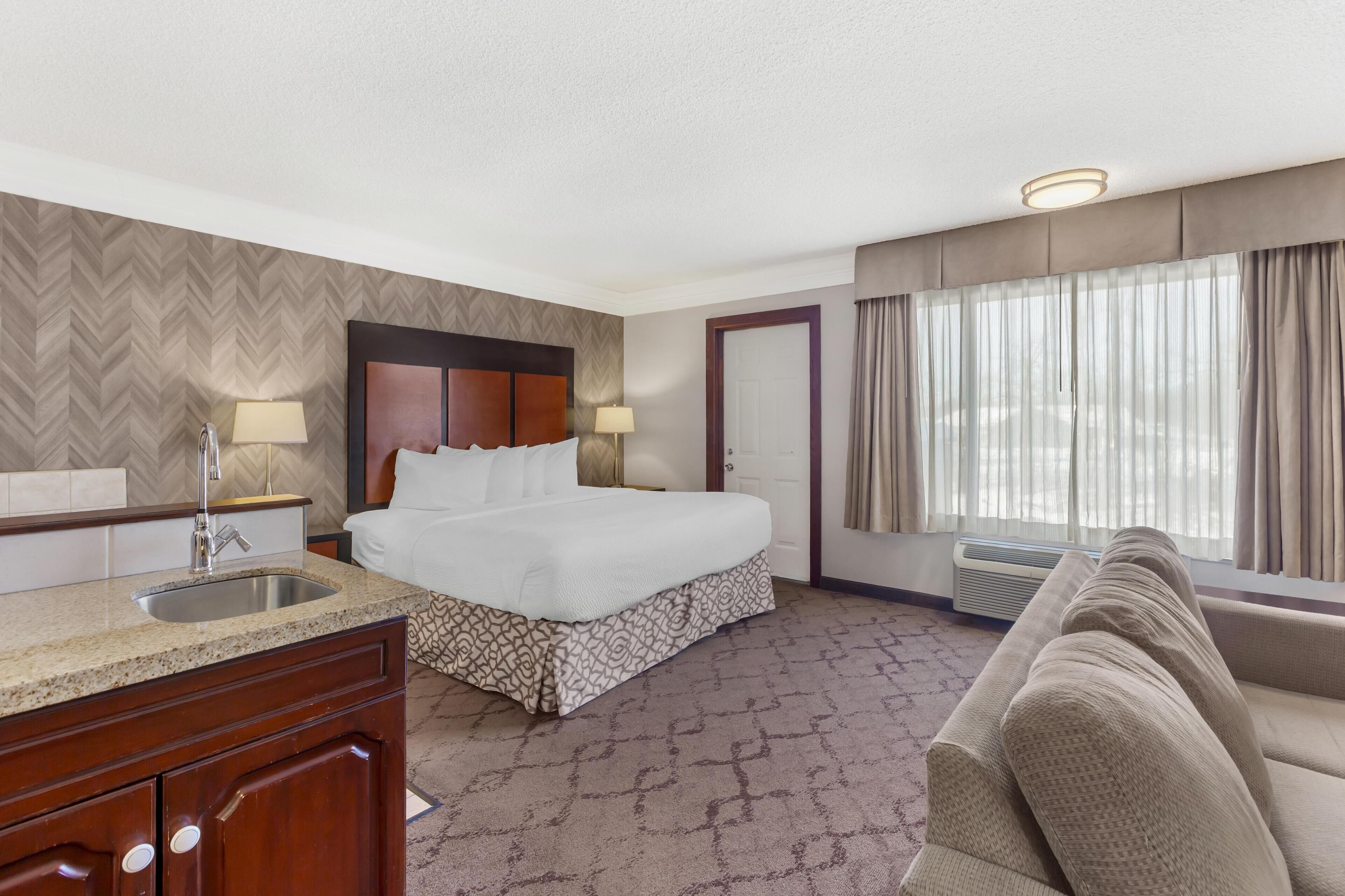 A hotel room with a bed, a sofa, a sink, and a window with curtains.