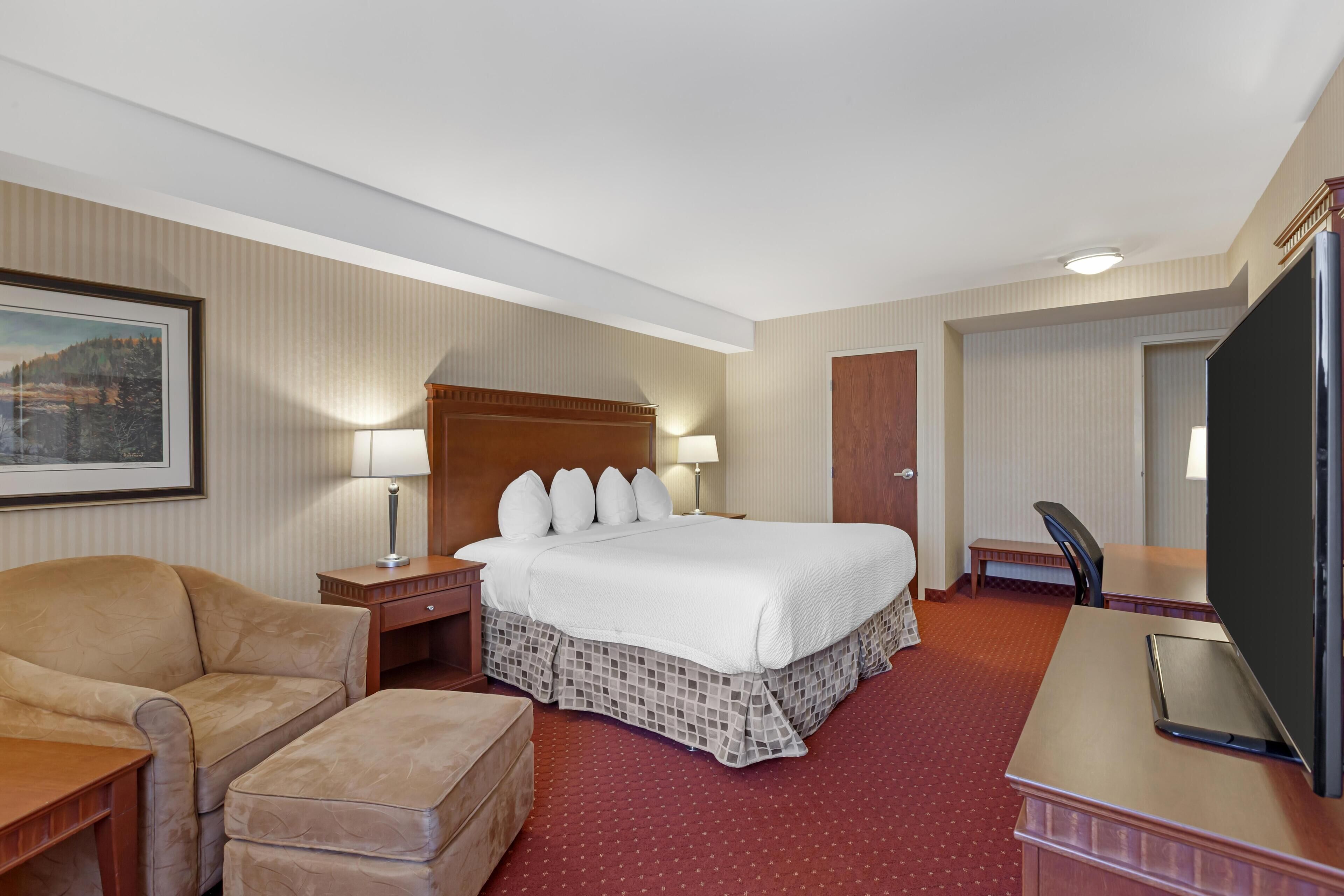 Ein Hotelzimmer mit einem großen Bett, einem Schreibtisch mit Computer, einem Sessel, einem kleinen Tisch und einem Fernseher.