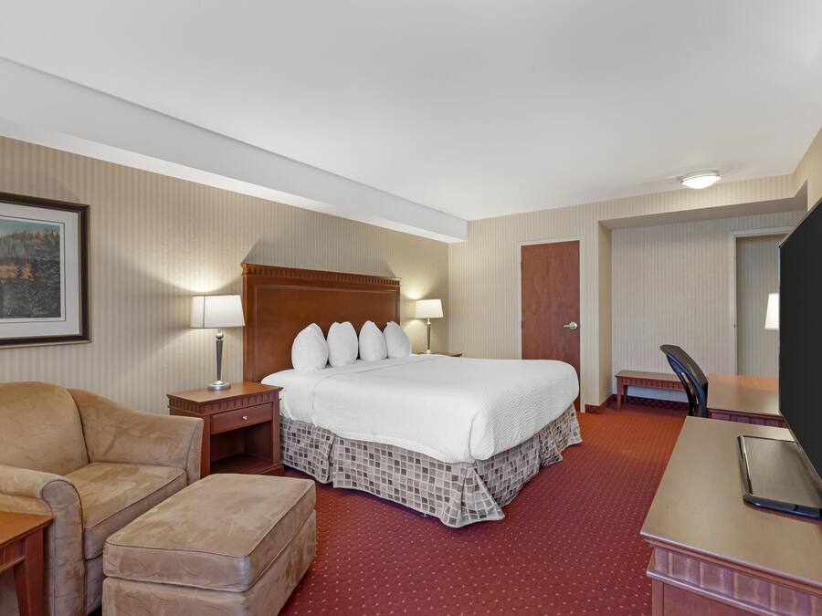 Ein Hotelzimmer mit einem großen Bett, einem Schreibtisch mit Computer, einem Sessel, einem kleinen Tisch und einem Fernseher.