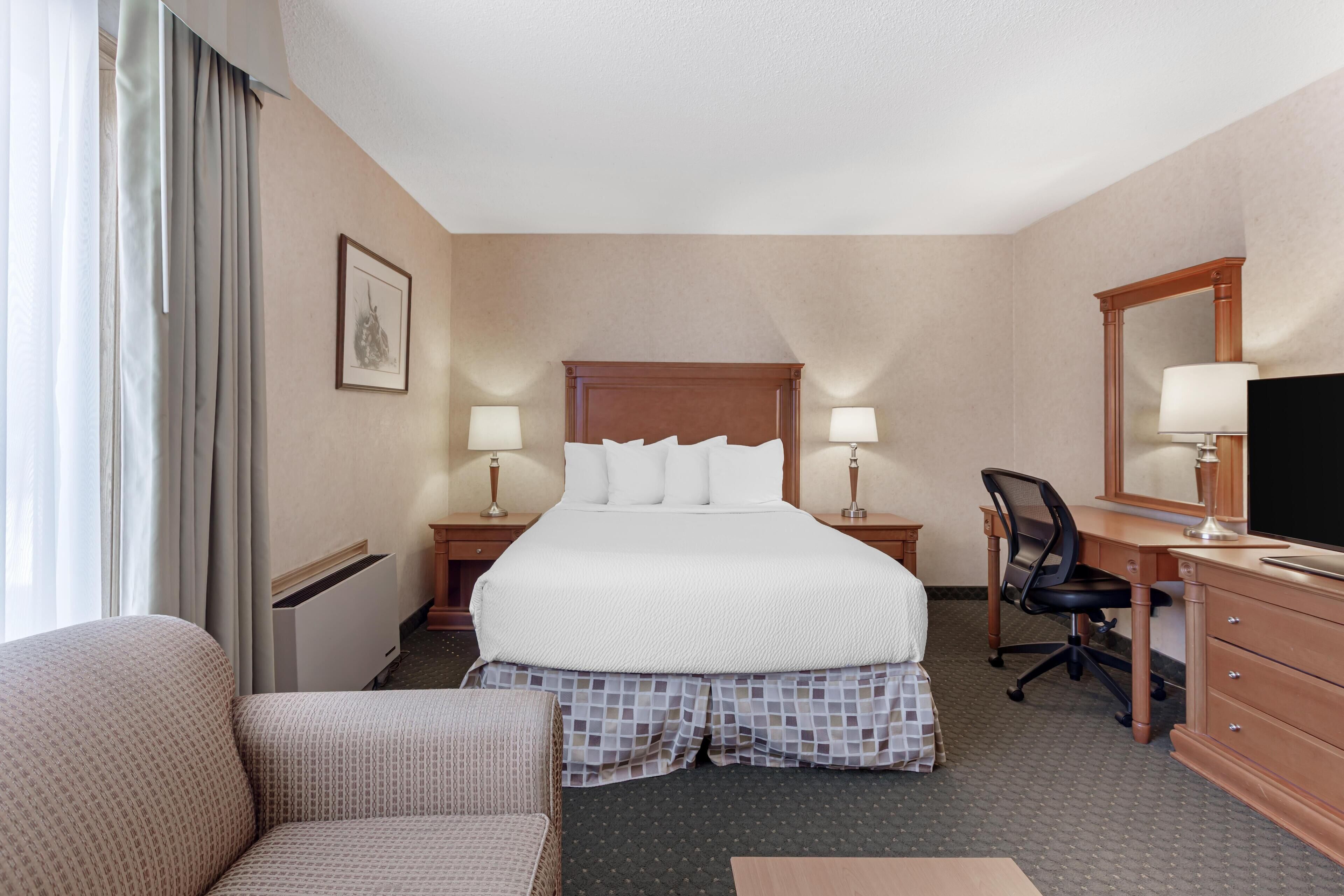 A hotel room with a large bed, two bedside tables with lamps, a desk with a chair, a dresser, and a large mirror.