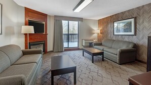 Habitación de hotel con sofá, mesa de centro, televisor, chimenea, balcón y un cuadro en la pared.