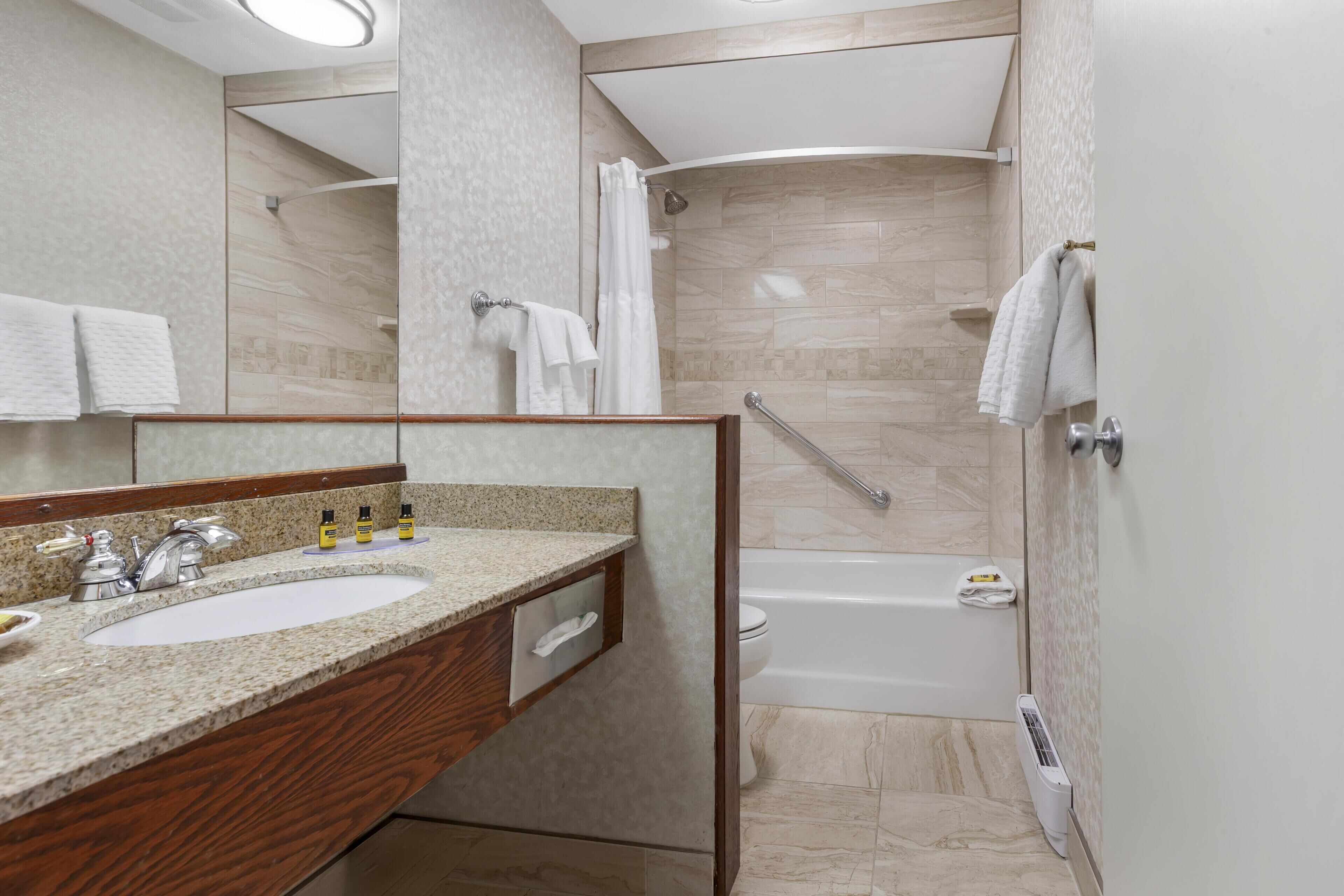 Un baño moderno con encimera de granito, un lavamanos, un espejo, una ducha y una bañera.