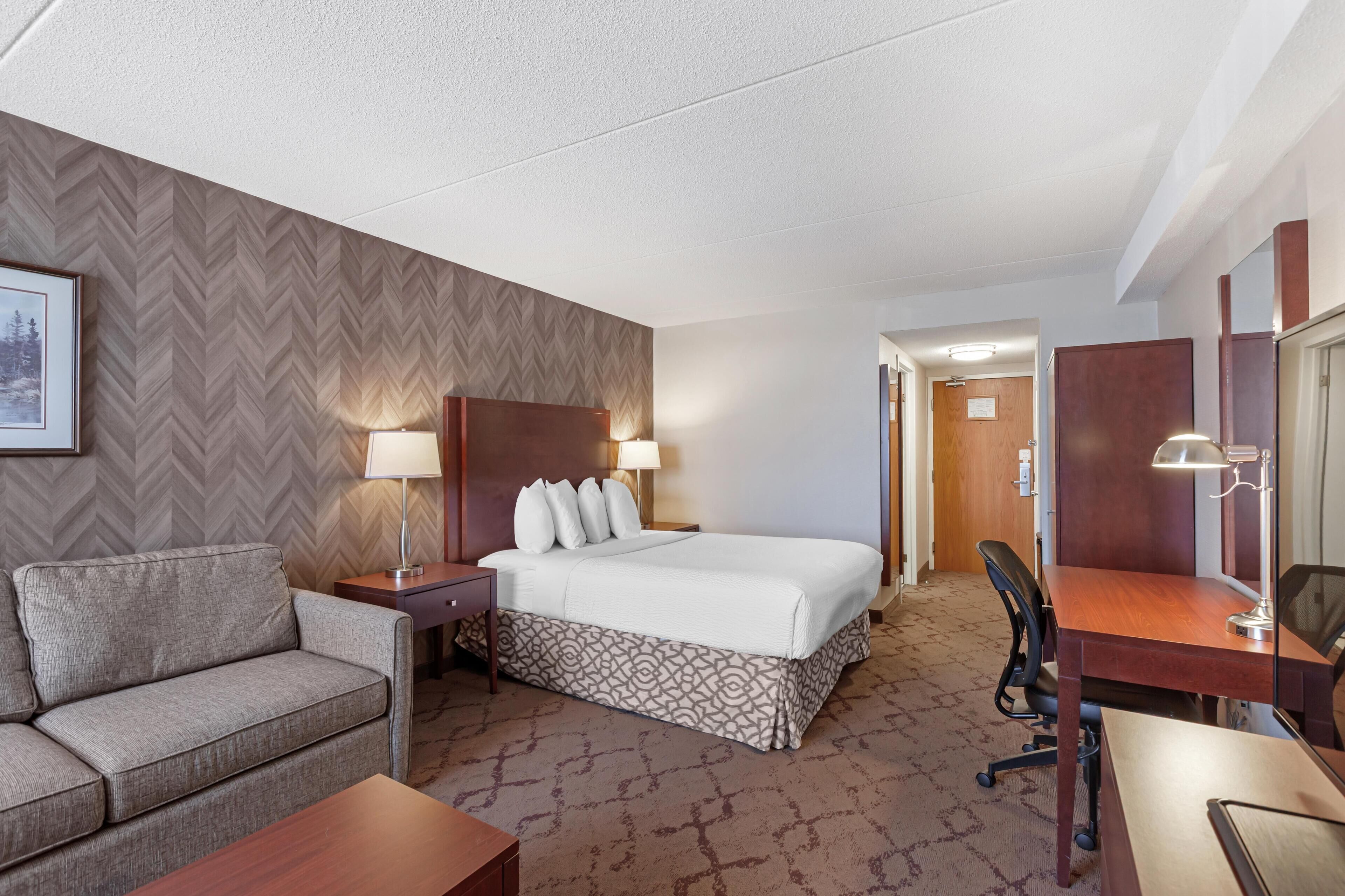 A hotel room with a bed, a sofa, a desk, and a chair.