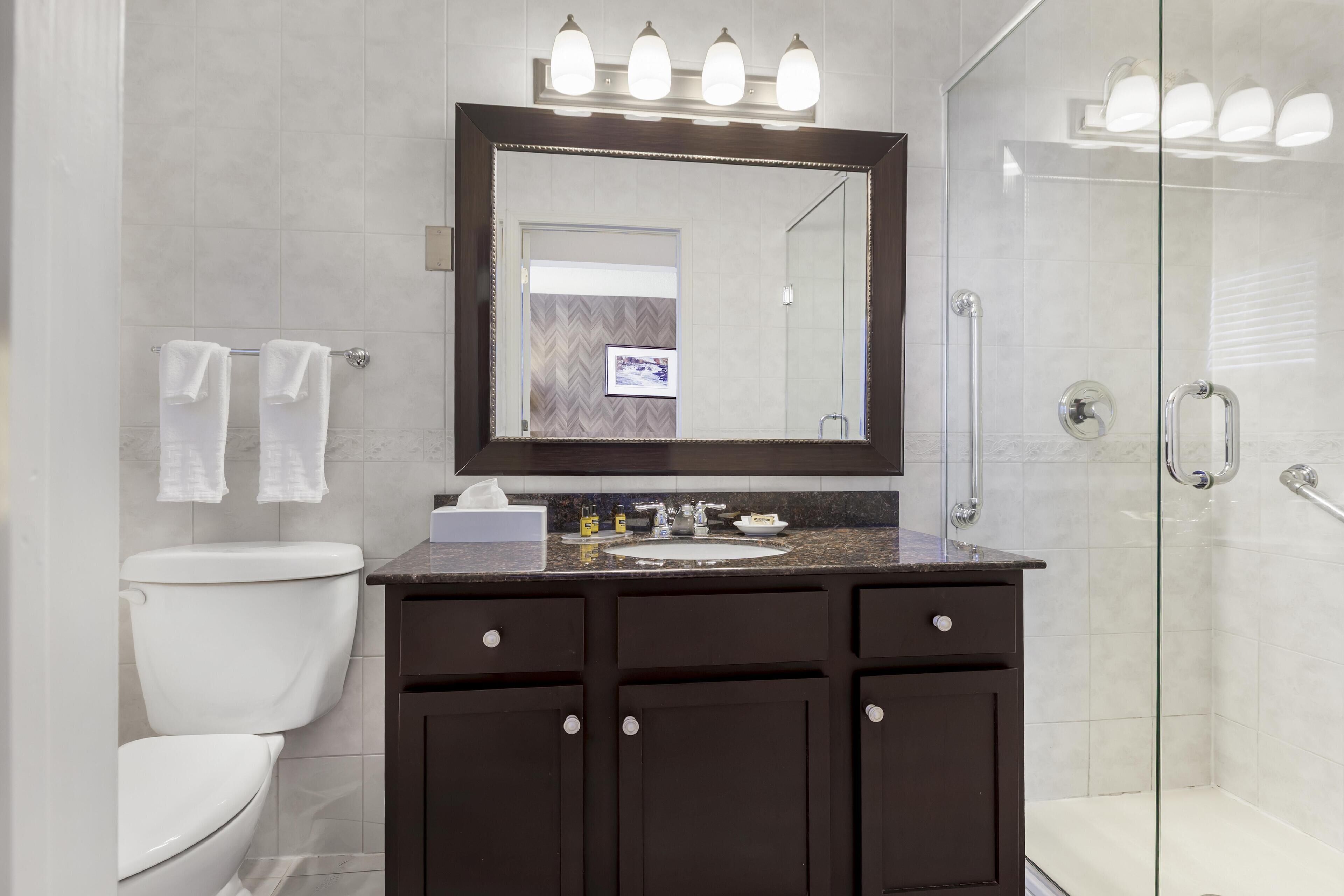 A modern bathroom with a dark vanity, a large mirror, and a glass-enclosed shower.