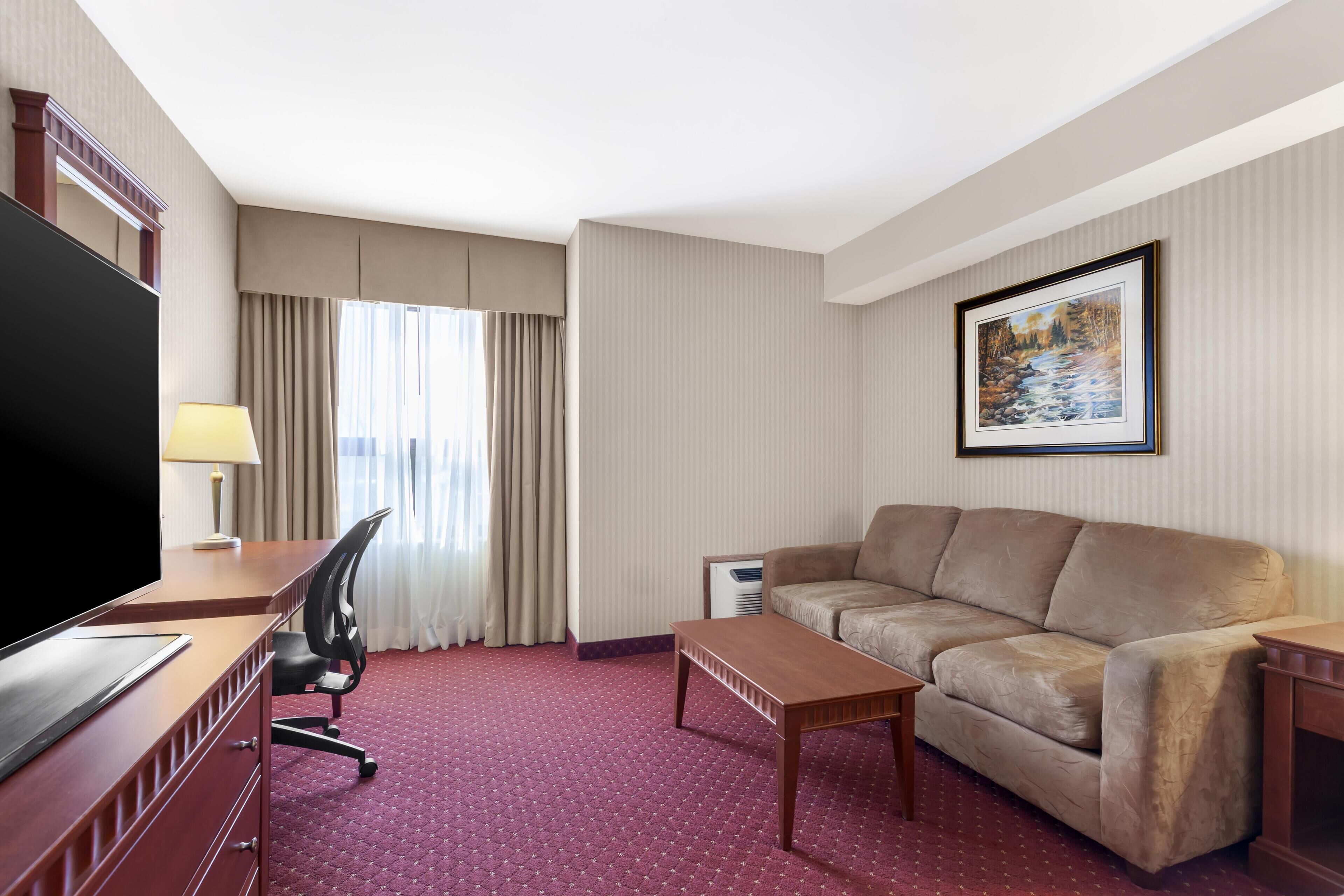 Habitación de hotel con televisor de pantalla plana grande, sofá, escritorio con silla, mesa de centro y un cuadro en la pared.