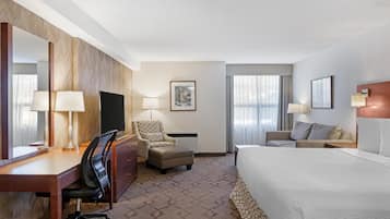 A hotel room with a large bed, a desk with a chair, a sofa, a chair, a TV, and a window with curtains.