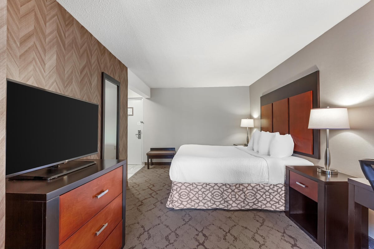 Ein Hotelzimmer mit einem großen Flachbildfernseher, einem Bett mit weißer Bettwäsche, einem gemusterten Teppich, einem Holz-Kopfteil und einem Schreibtisch mit einer Lampe.