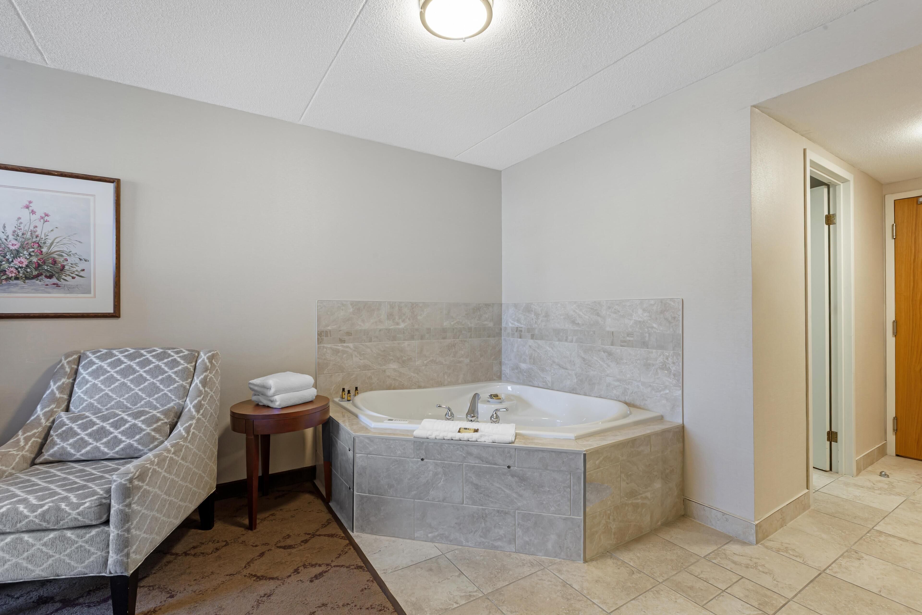 Un baño con una bañera grande, una silla y una mesita con una toalla y botellas.