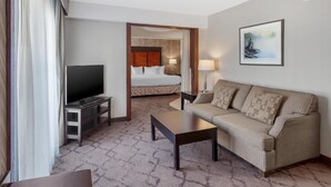 Habitación de hotel con cama, televisión, sofá, mesa de centro y un cuadro en la pared.