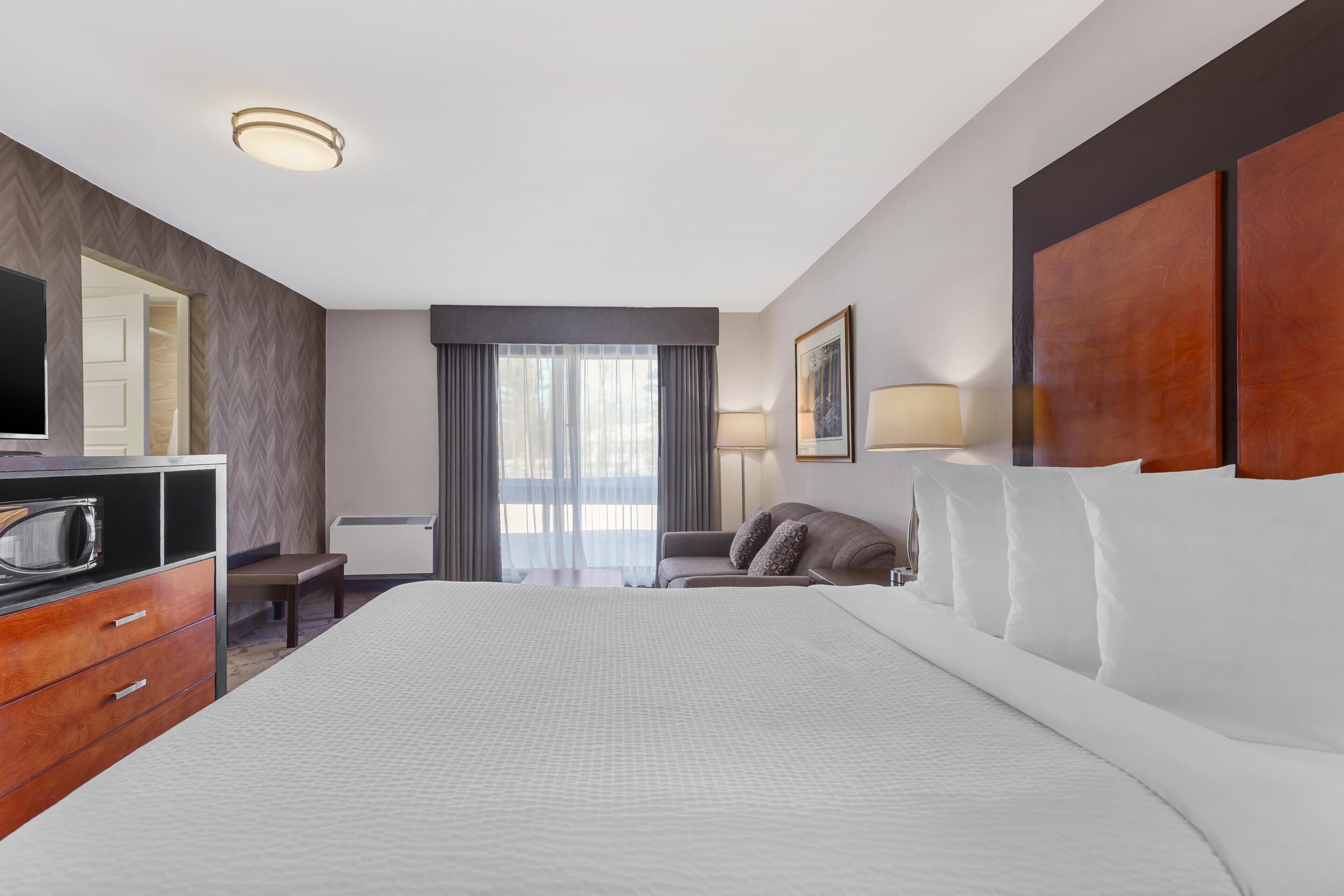 Een hotelkamer met een groot bed, een bureau met een computer, een stoel, een televisie en een raam met gordijnen.