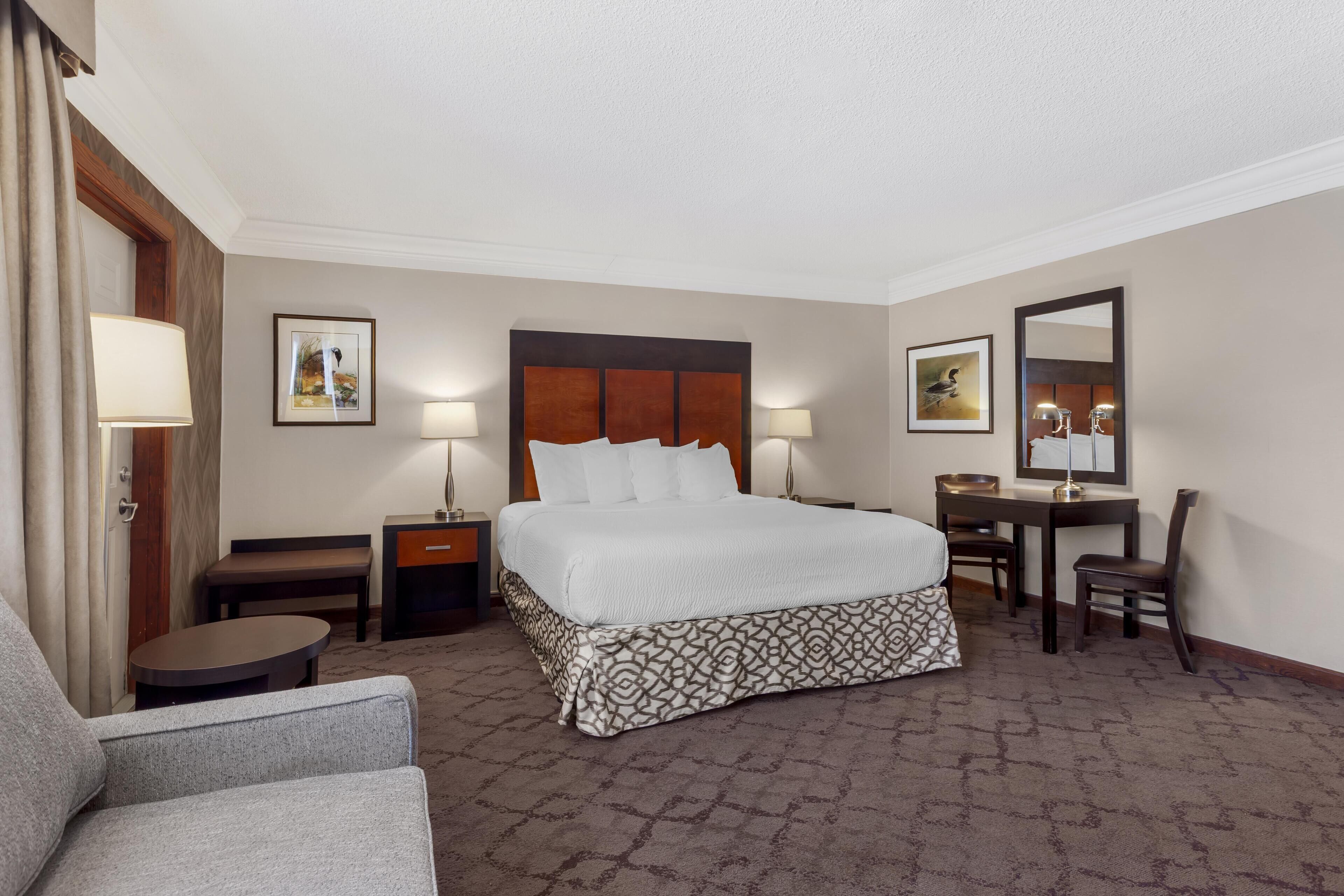 A hotel room with a large bed, bedside tables, a desk, a chair, and a lamp.