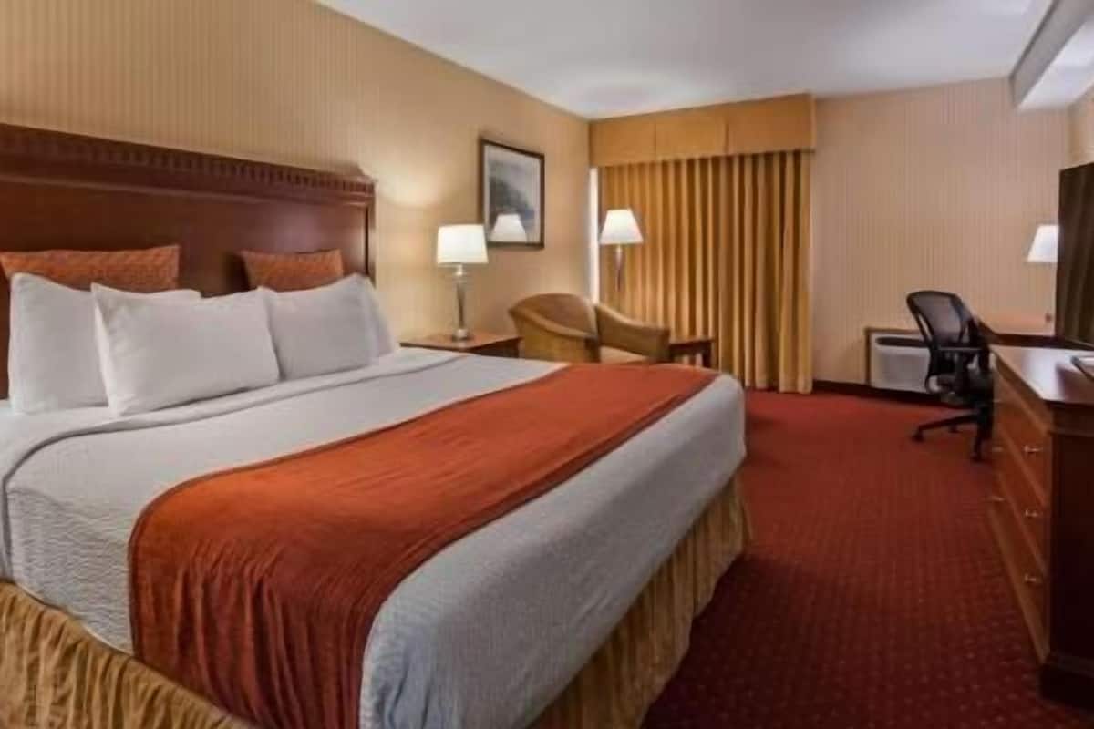 Ein Hotelzimmer mit einem großen Bett, einem Schreibtisch, einem Sessel und einem Fernseher.