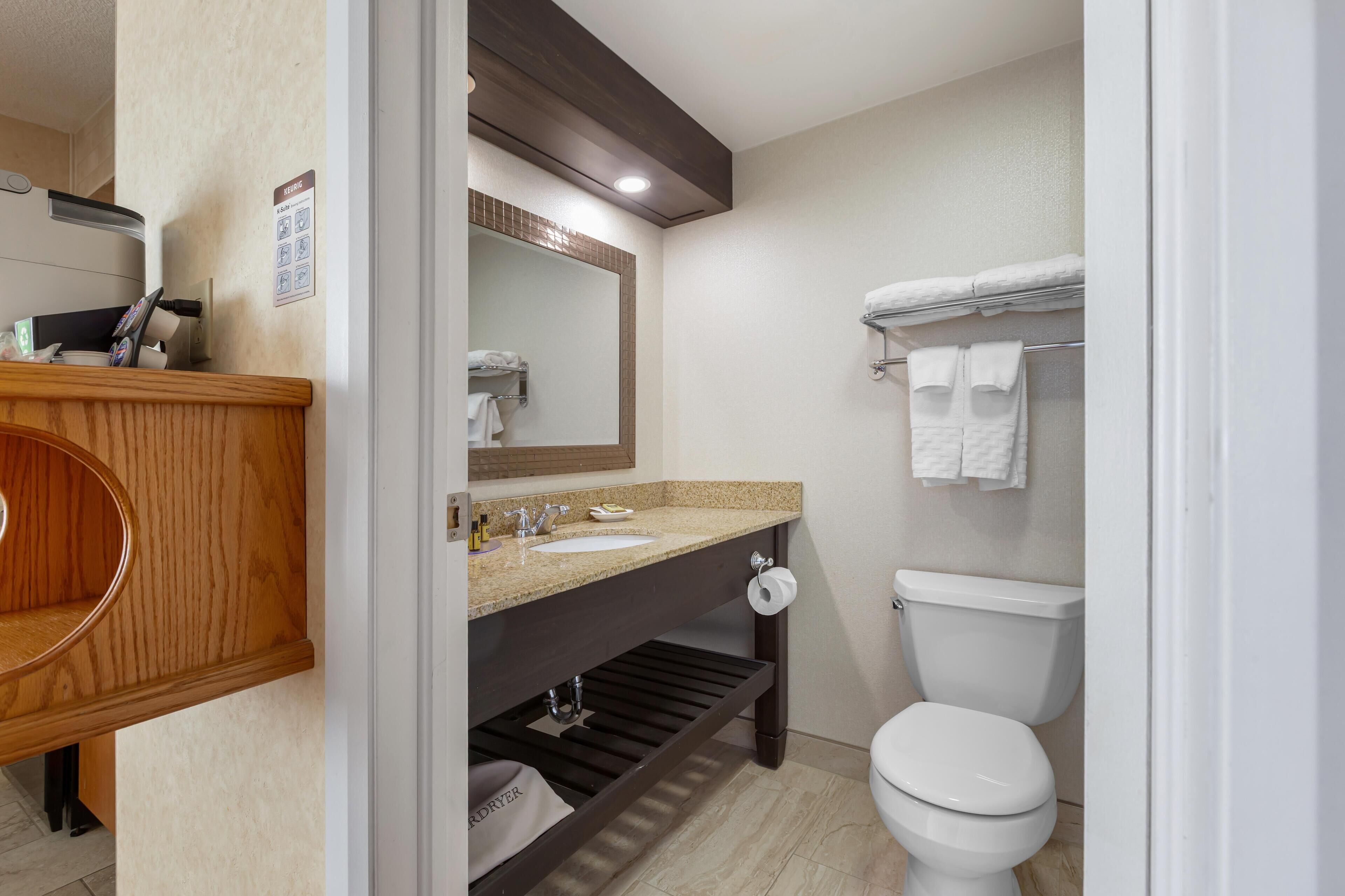 A modern bathroom with a wooden vanity, two sinks, a toilet, and a towel rack.