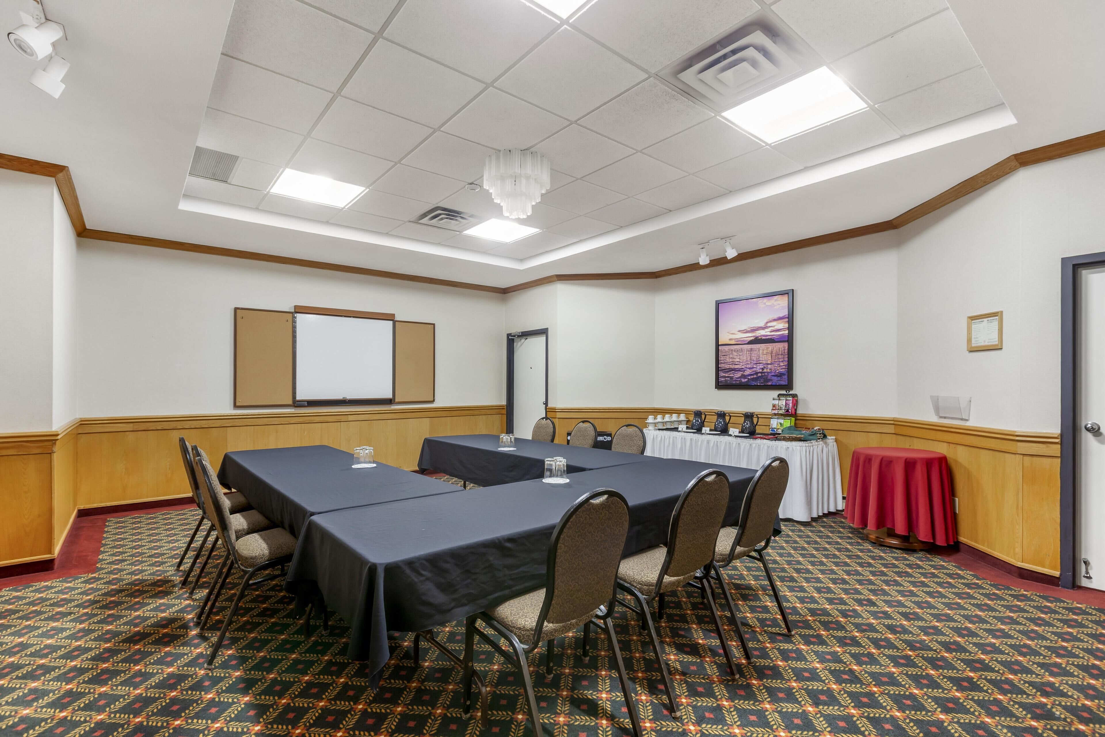 Un salón de conferencias con una gran mesa, sillas, una pantalla de proyector y un mantel rojo.