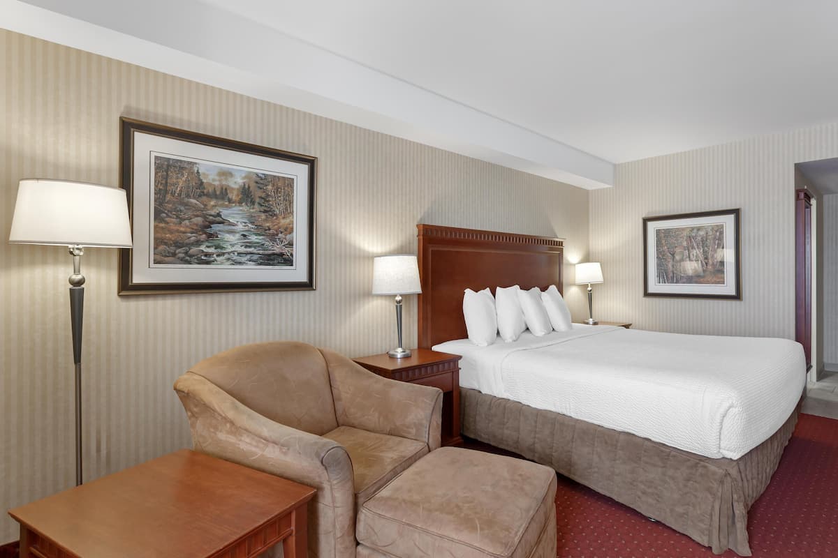 Ein Hotelzimmer mit einem Bett, einem Sessel, einem Schreibtisch und zwei Lampen.