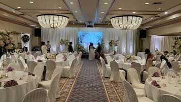 A banquet hall with round tables, white chairs, and chandeliers.