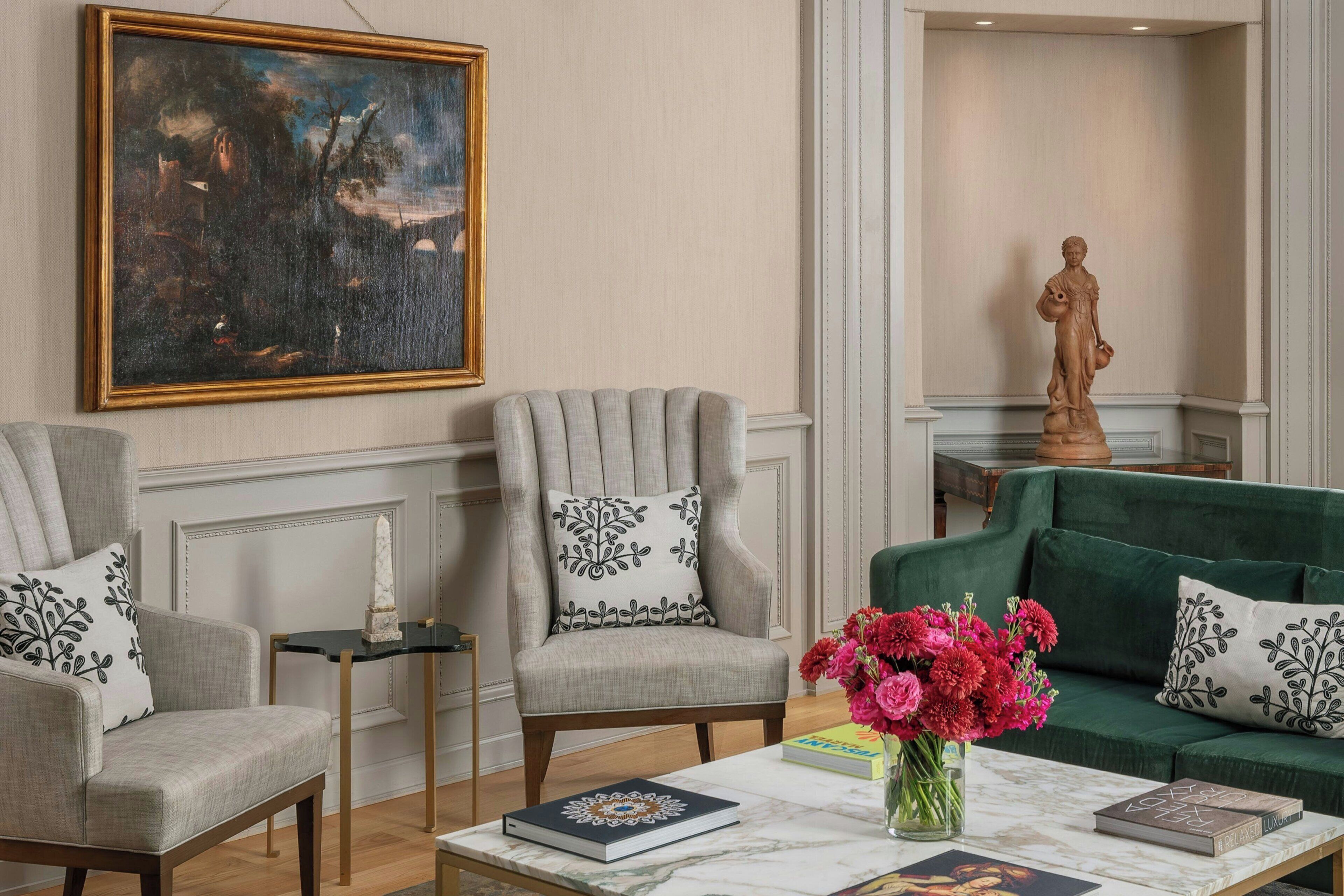 A living room with two armchairs, a green sofa, a marble coffee table, a painting, and a statue.
