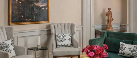 A living room with two armchairs, a green sofa, a marble coffee table, a painting, and a statue.
