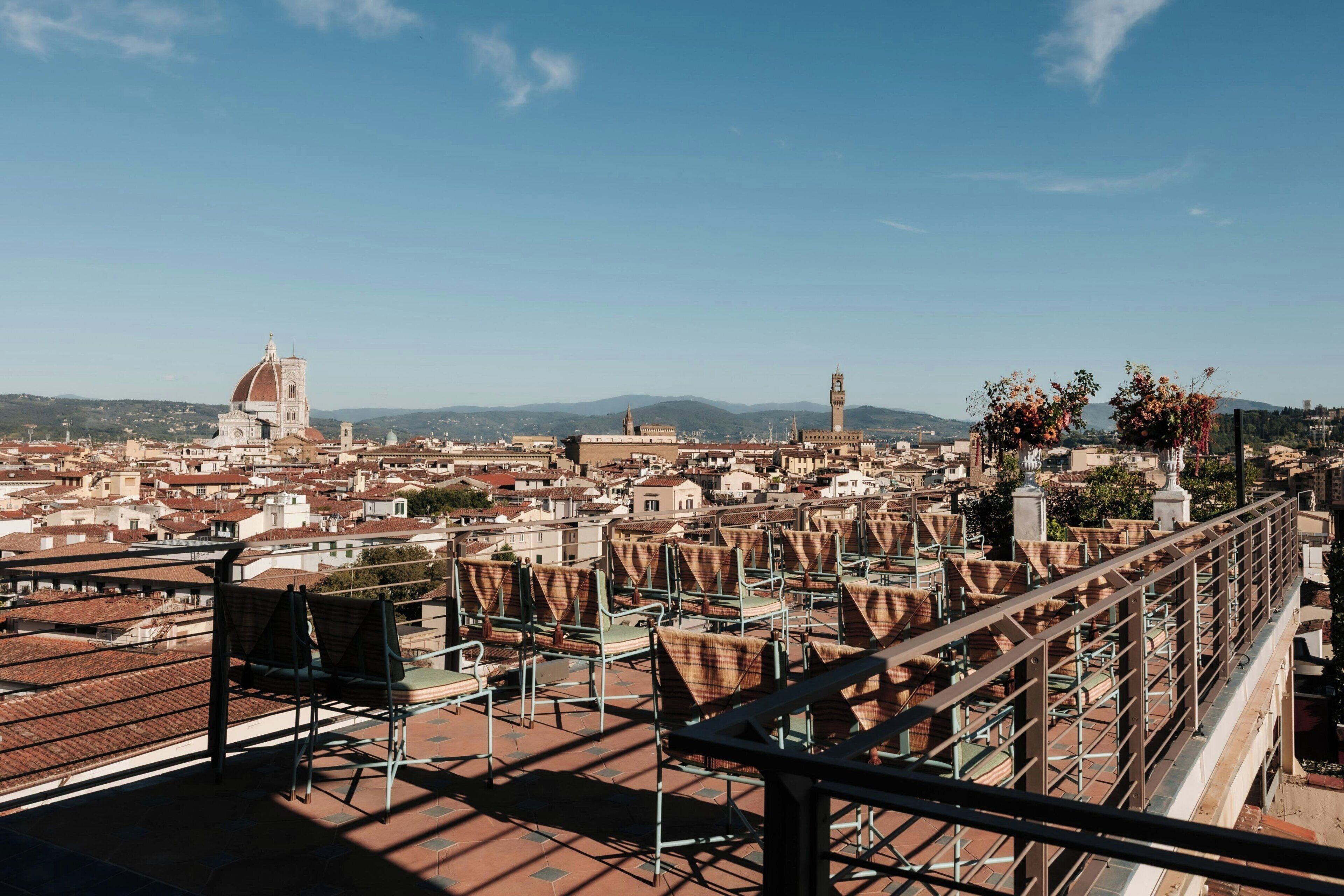 A cityscape with a prominent dome and tower, a balcony with chairs, and a clear sky.