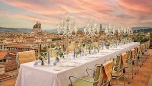 A long table set for a meal with a cityscape view in the background. - The Excelsior, a Luxury Collection Hotel, Florence (Florence)