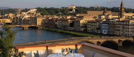 A terrace with a table set for dining, overlooking a cityscape with a river and historic buildings.