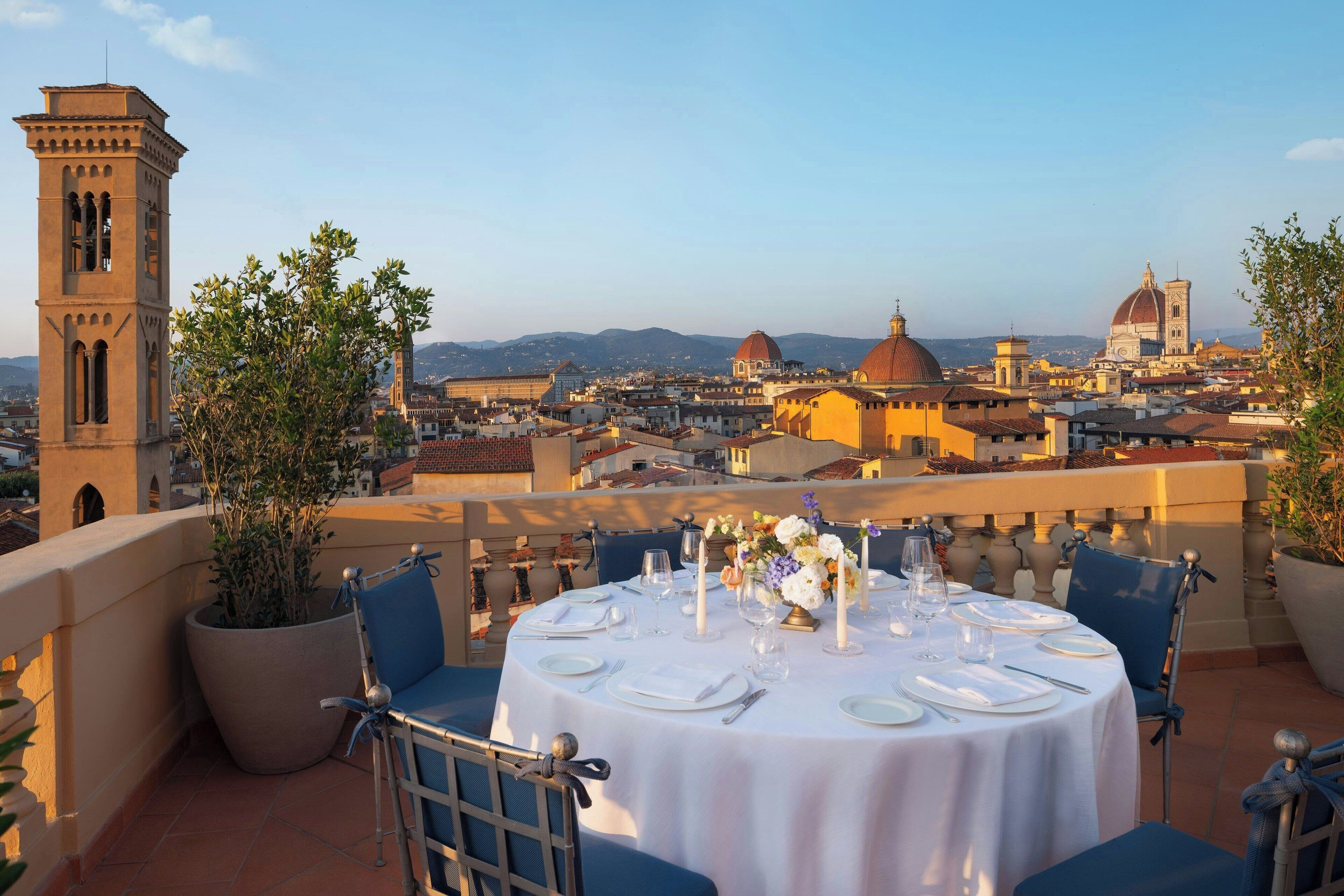 A rooftop terrace with a table set for dining, overlooking a cityscape with historic buildings and a tower.