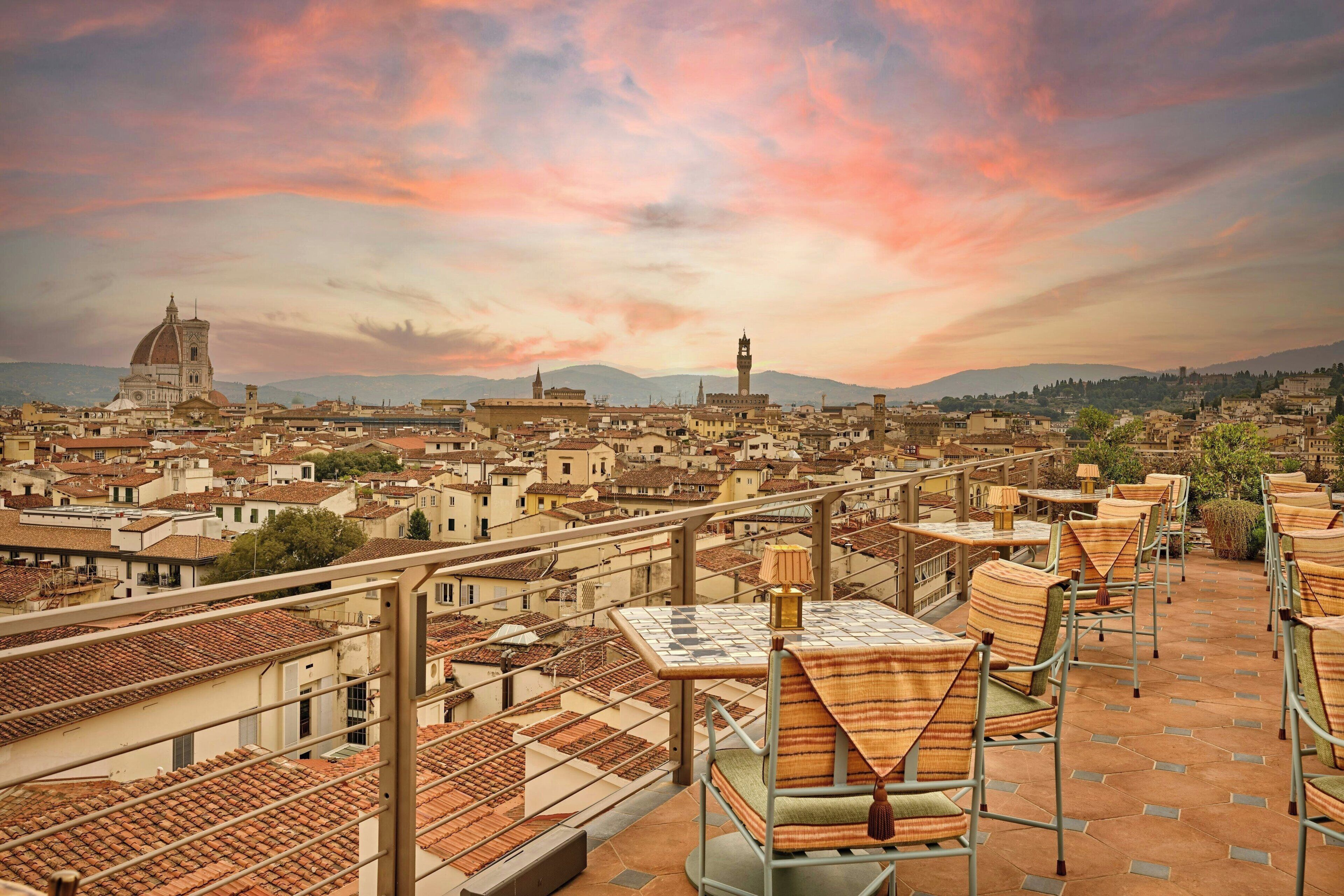 A terrace with tables and chairs, overlooking a cityscape with historic buildings and a prominent dome structure.