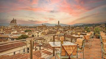 A terrace with tables and chairs, overlooking a cityscape with historic buildings and a prominent dome structure.