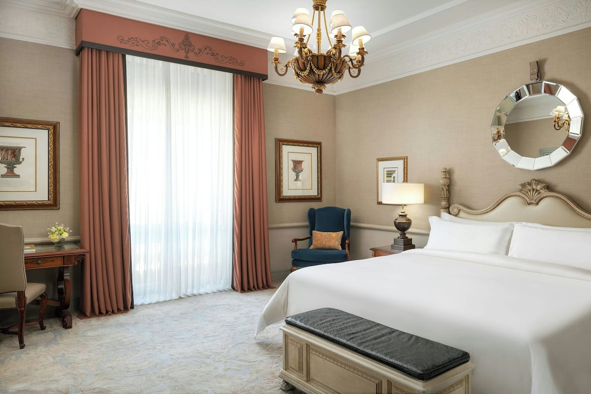 A hotel room with a large bed, a desk, a chair, a desk lamp, and a mirror on the wall.