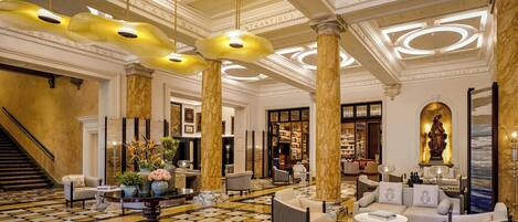 A spacious lobby with a checkered floor, marble columns, and a grand staircase.