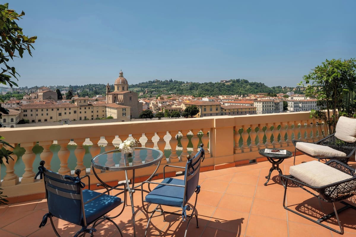 A terrace with a round table and two chairs, overlooking a cityscape with historic buildings and a hill in the distance.