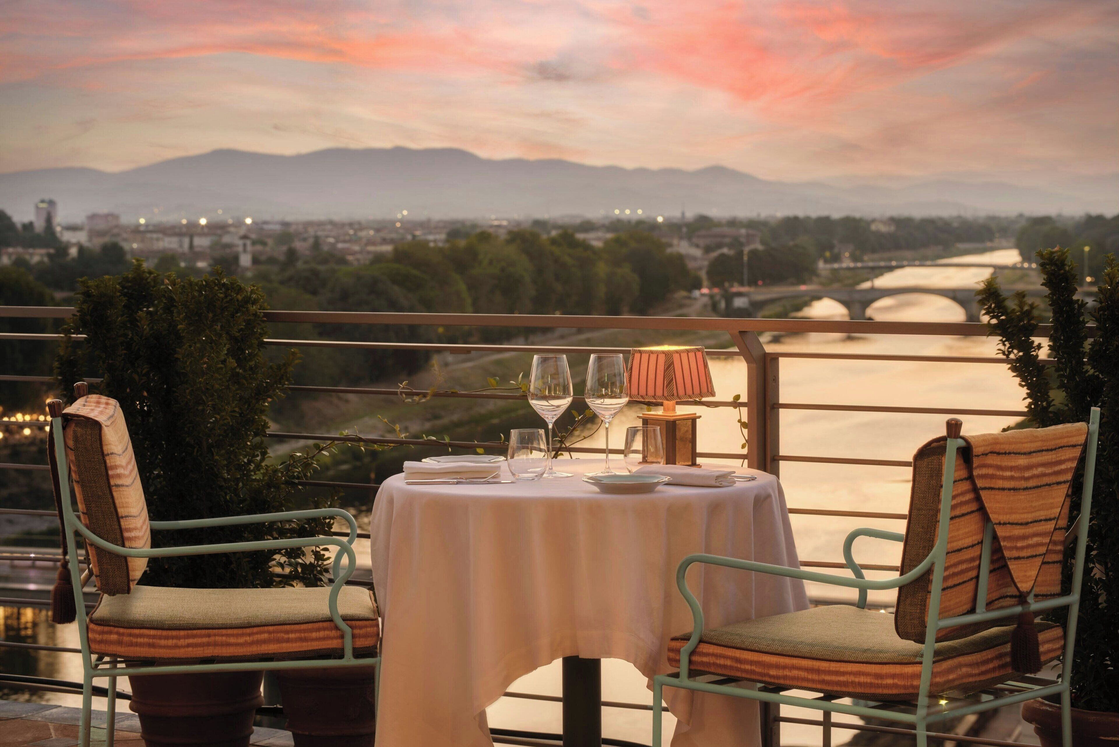 Un comedor con una mesa lista para dos, con vistas a un paisaje urbano y montañas.