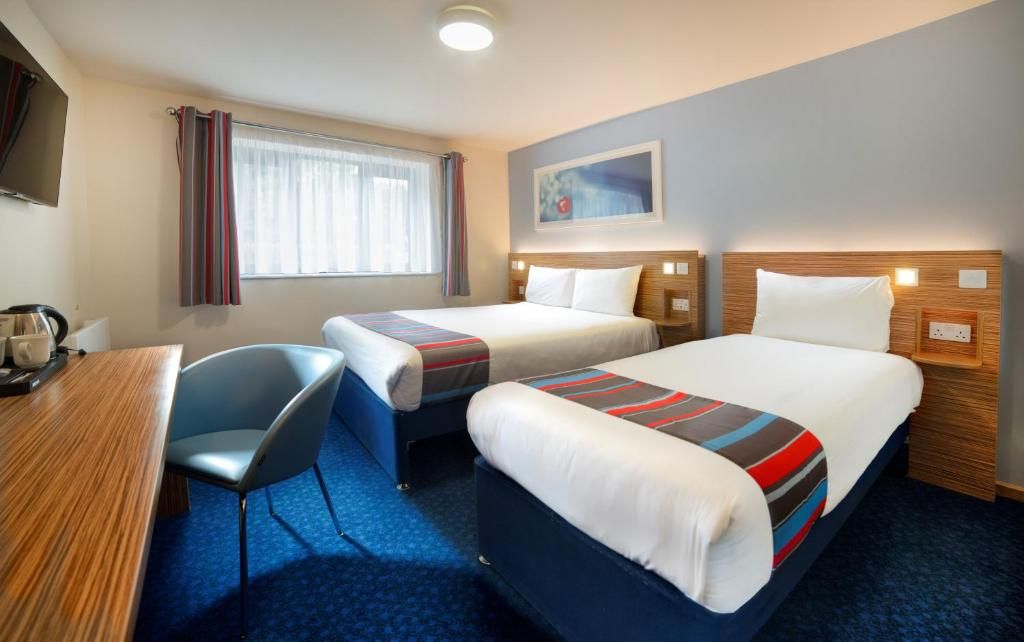 A hotel room with two beds, a desk, and a chair.