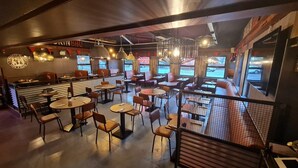Un restaurante amplio con varias zonas de estar, incluyendo mesas redondas y cabinas, y vista al estacionamiento a través de amplias ventanas.