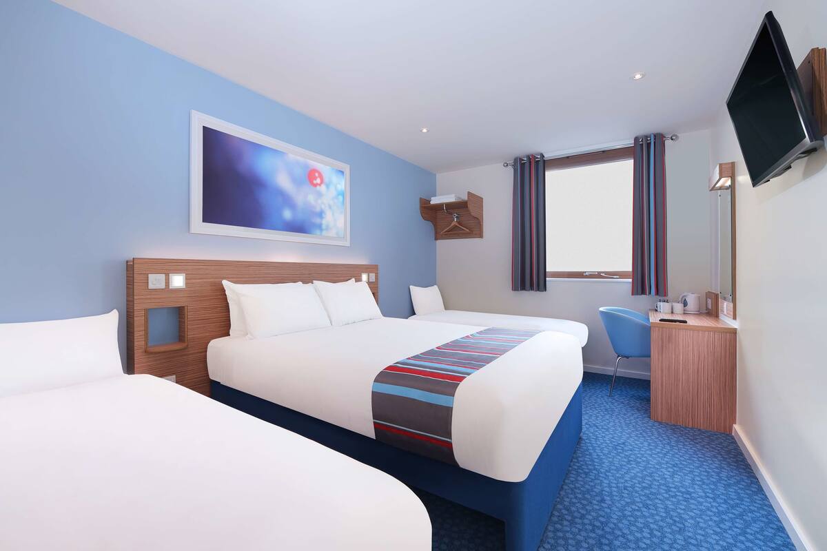 A hotel room with two beds, a desk, a chair, a TV, and a window with curtains.