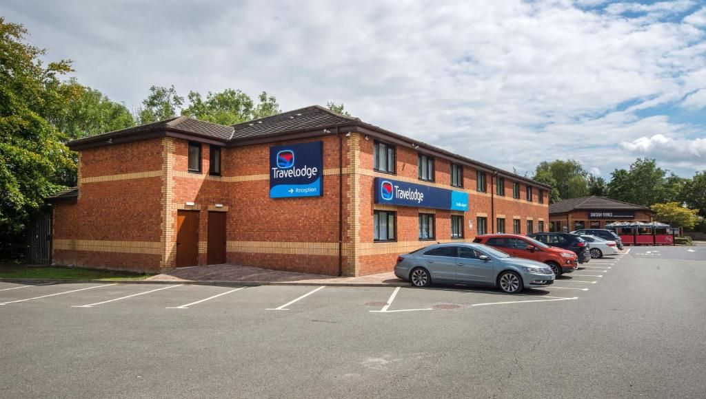 A Travelodge hotel with a brick facade, multiple parking spaces, and a clear sky.