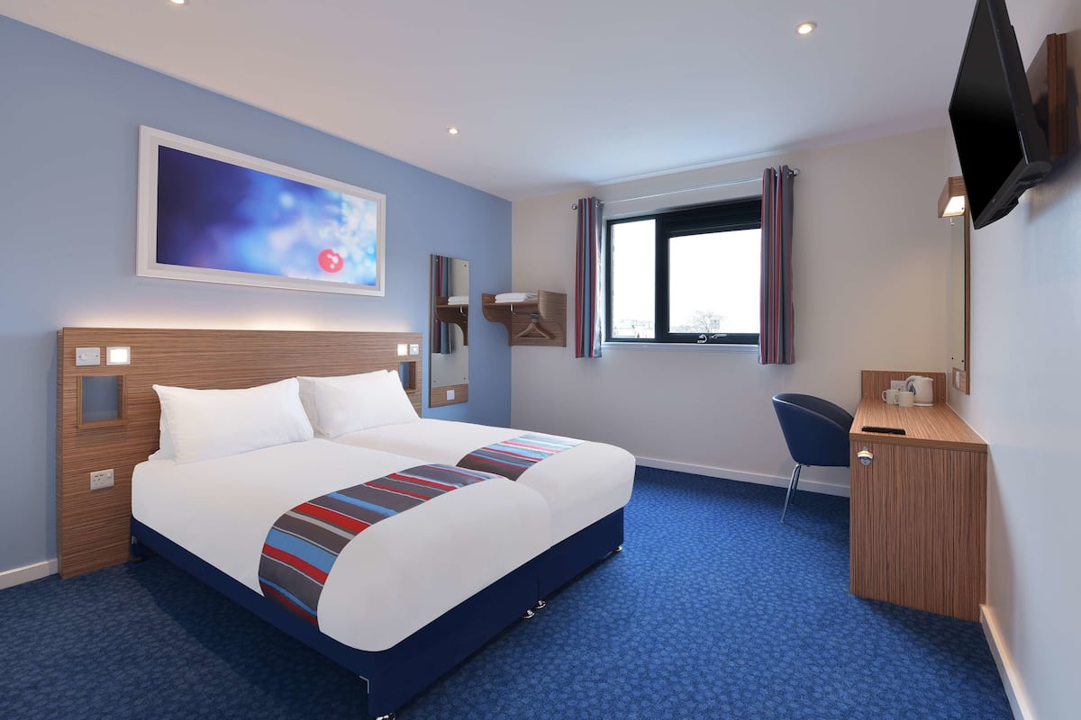 A hotel room with a large bed, a desk, a chair, and a TV mounted on the wall.
