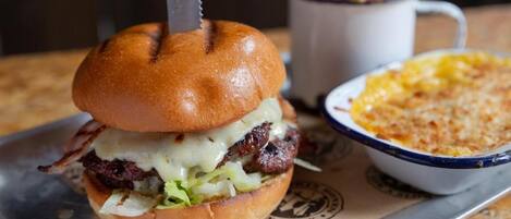 Una hamburguesa con un cuchillo encima, una porción de papas fritas y un bol de macarrones con queso.