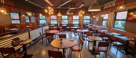 A restaurant interior with booths, round tables, and high ceiling lighting.