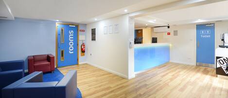 A reception area with a blue sign reading "rooms," a reception desk, a blue "Toilet" sign, and a fire extinguisher on the wall.