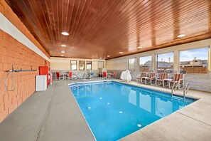 An indoor swimming pool with a wooden ceiling, red brick walls, and a view of a building outside.