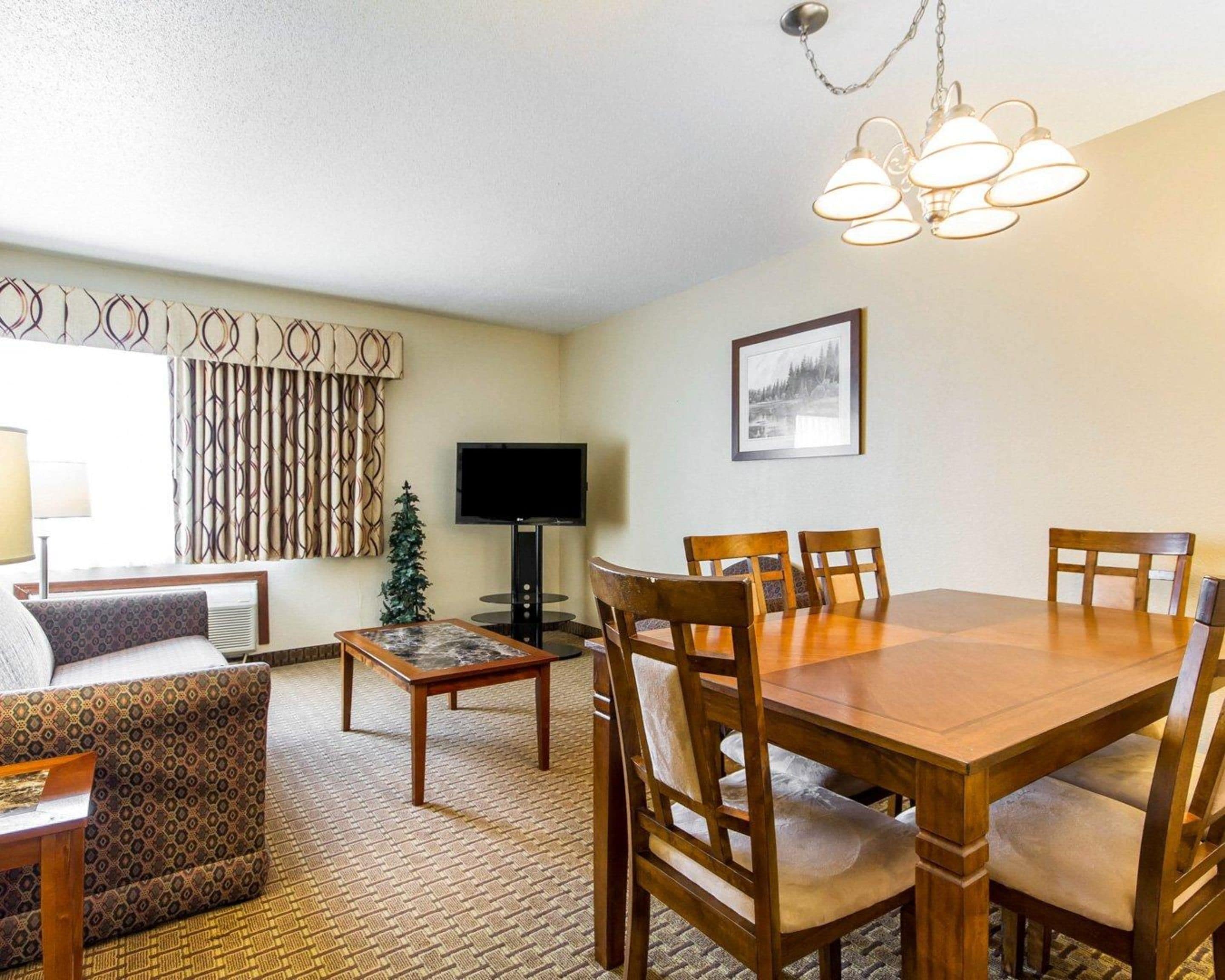 A hotel room with a dining table, chairs, a television, a small Christmas tree, and a patterned curtain.