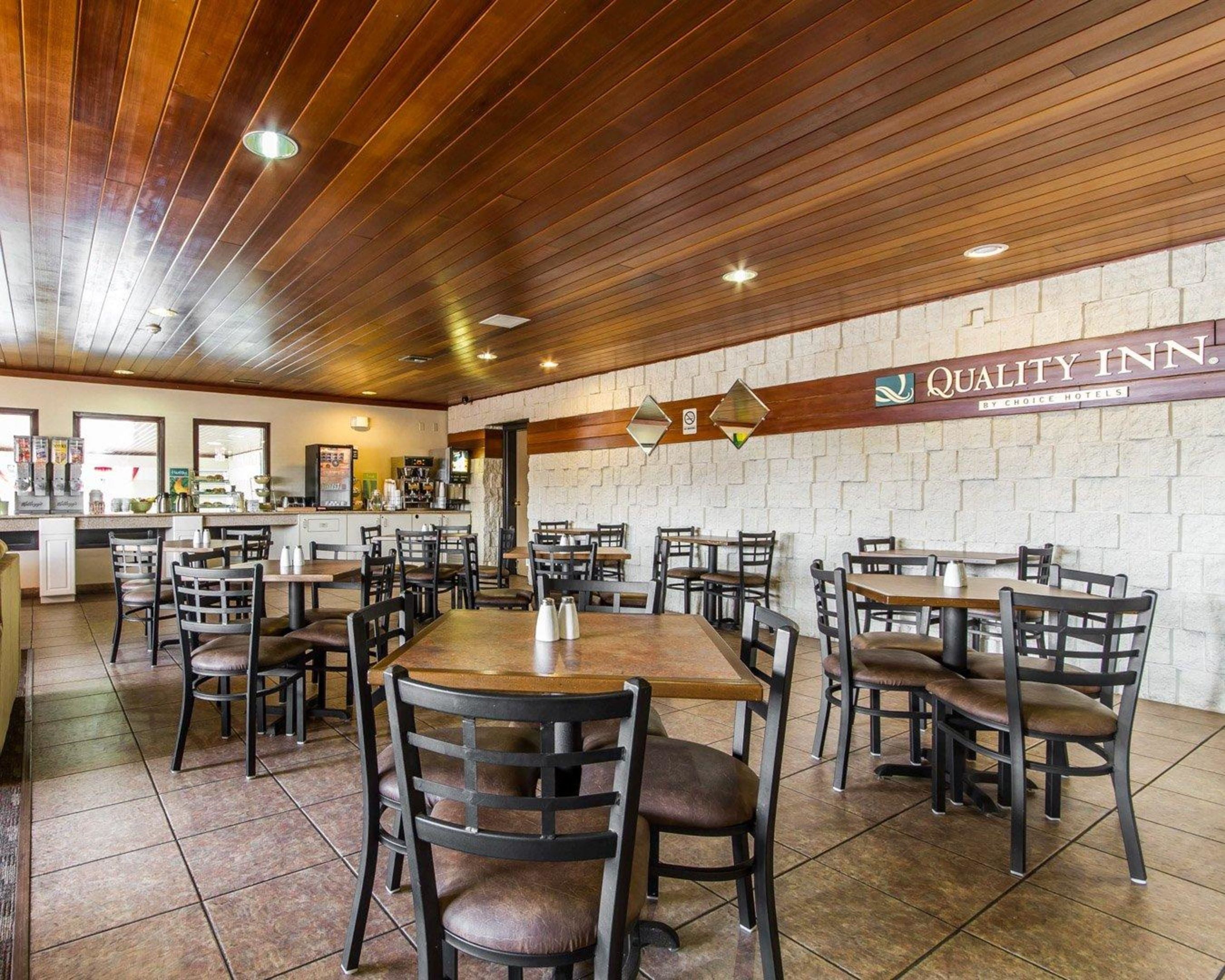A restaurant with wooden ceiling and brick walls, featuring tables and chairs arranged for dining.