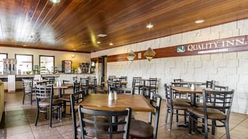 A restaurant with wooden ceiling and brick walls, featuring tables and chairs arranged for dining.