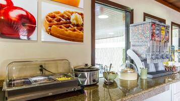 A breakfast buffet area with a self-service station, a waffle station, and a beverage dispenser.